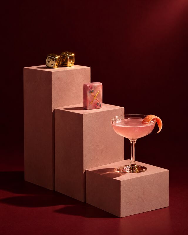 Brass dice and a pink cocktail on plinths