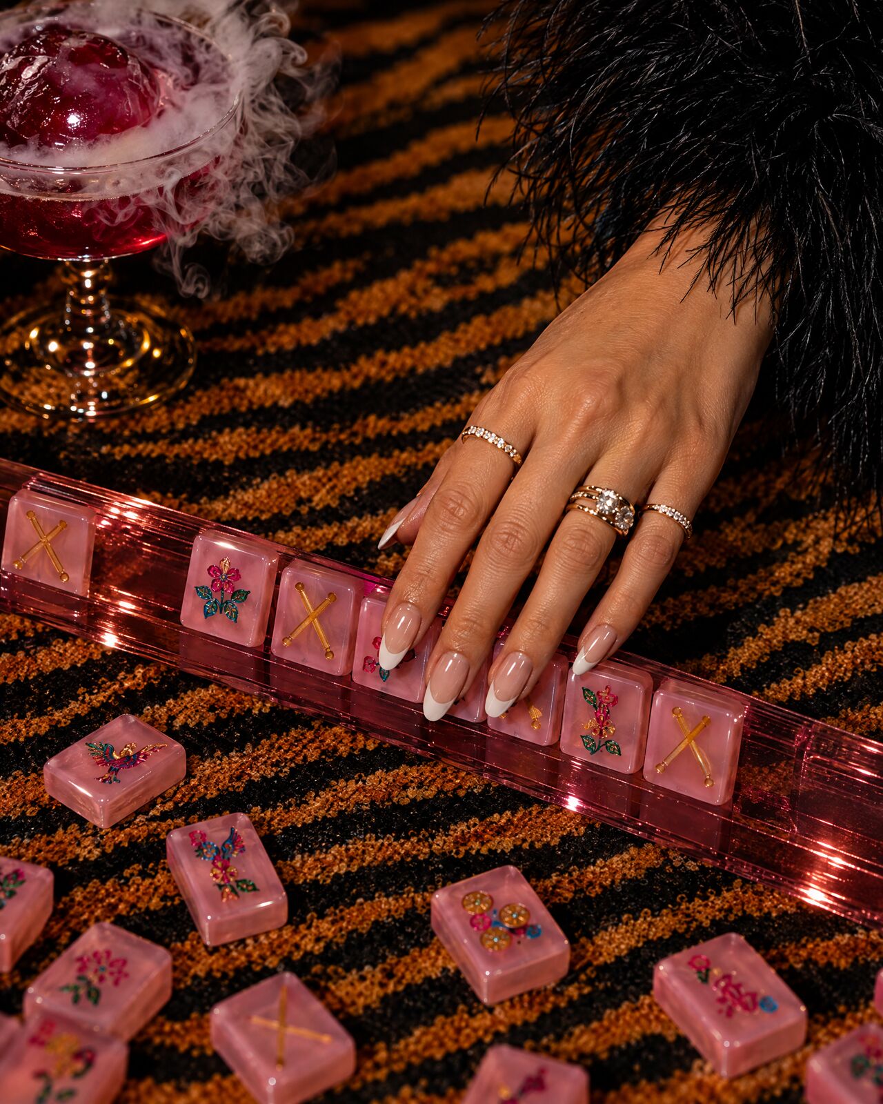 A hand with gold rings sliding pink tiles along a rack on a tiger-stripe mat