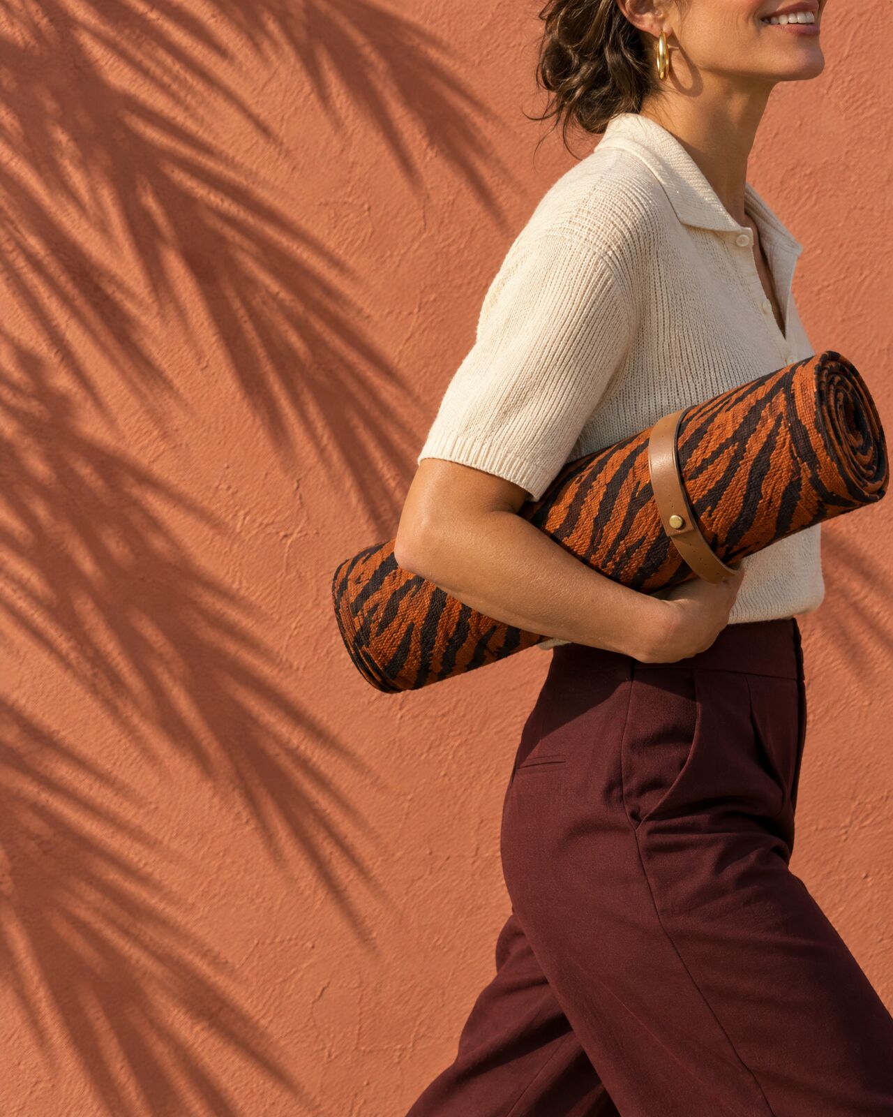 A rolled tiger-stripe mat carried under someone's arm against a terracotta wall