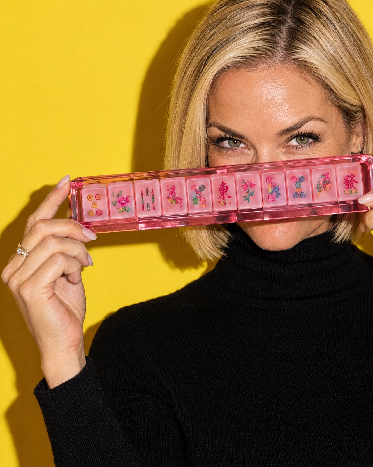 A woman holding a rack of pink tiles across her face, eyes peeking over it