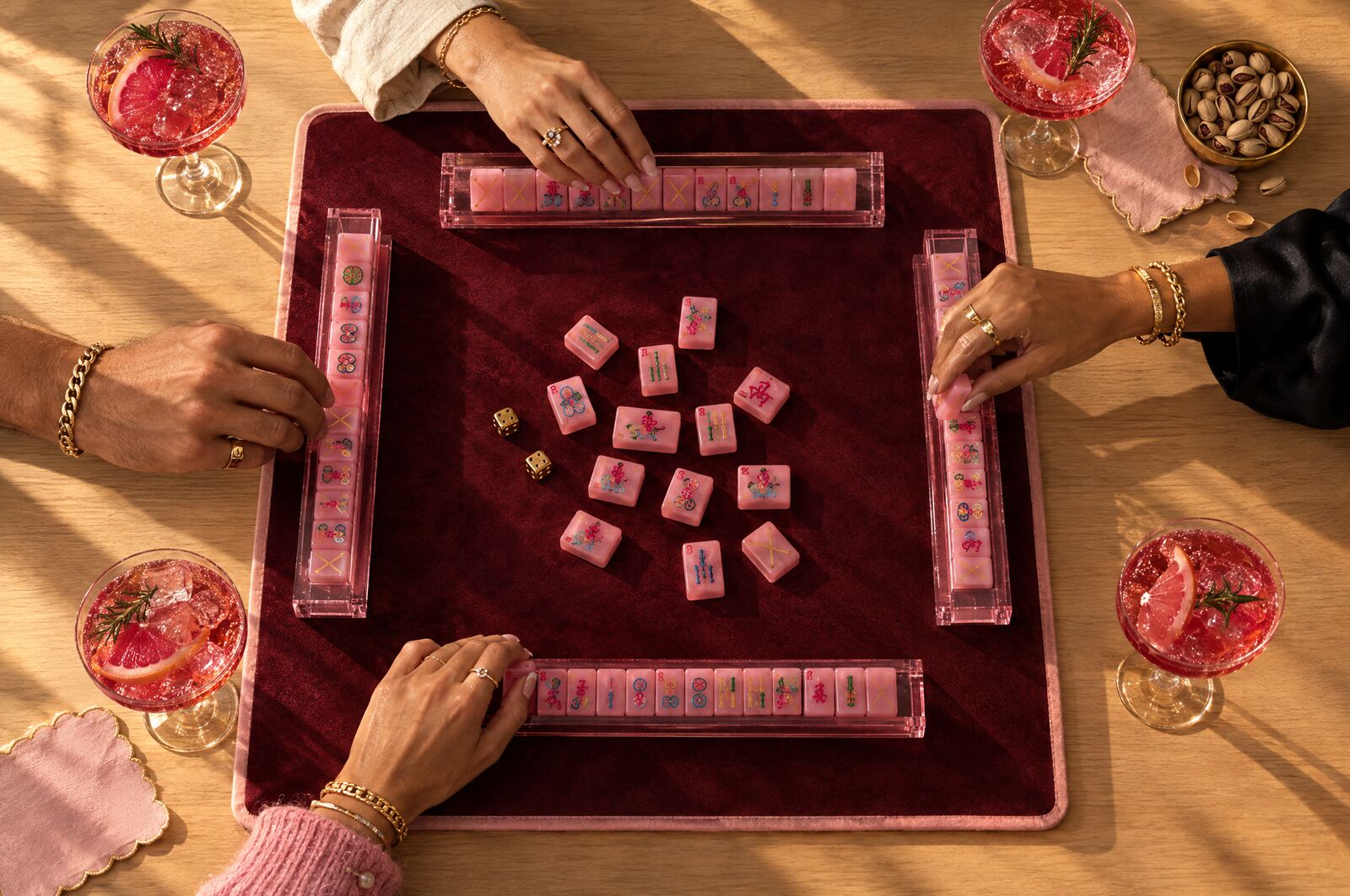 Four players' hands around the oxblood mat and pink racks, from above