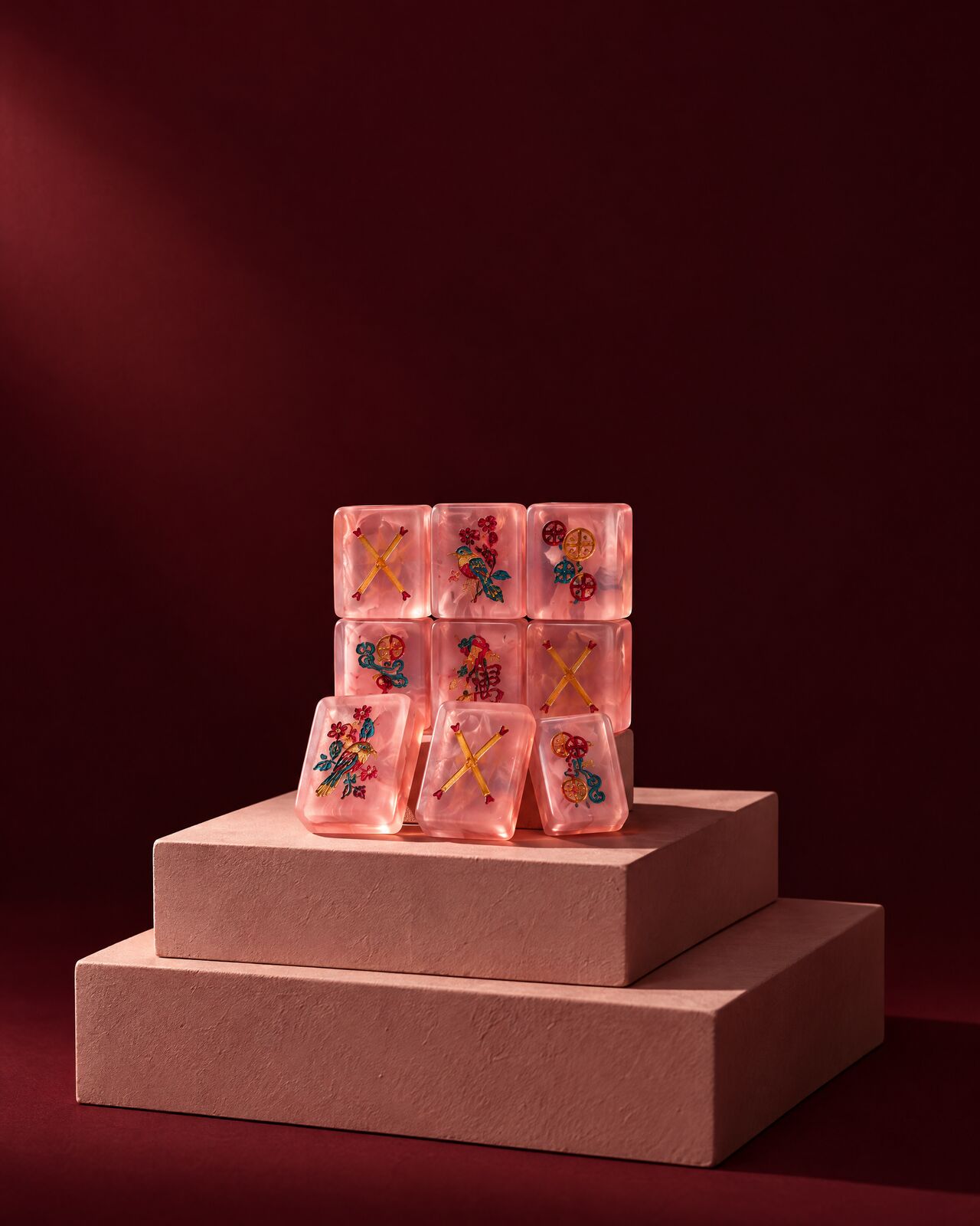 A small wall of frosted blush mahjong tiles on two stacked plaster plinths under a spotlight